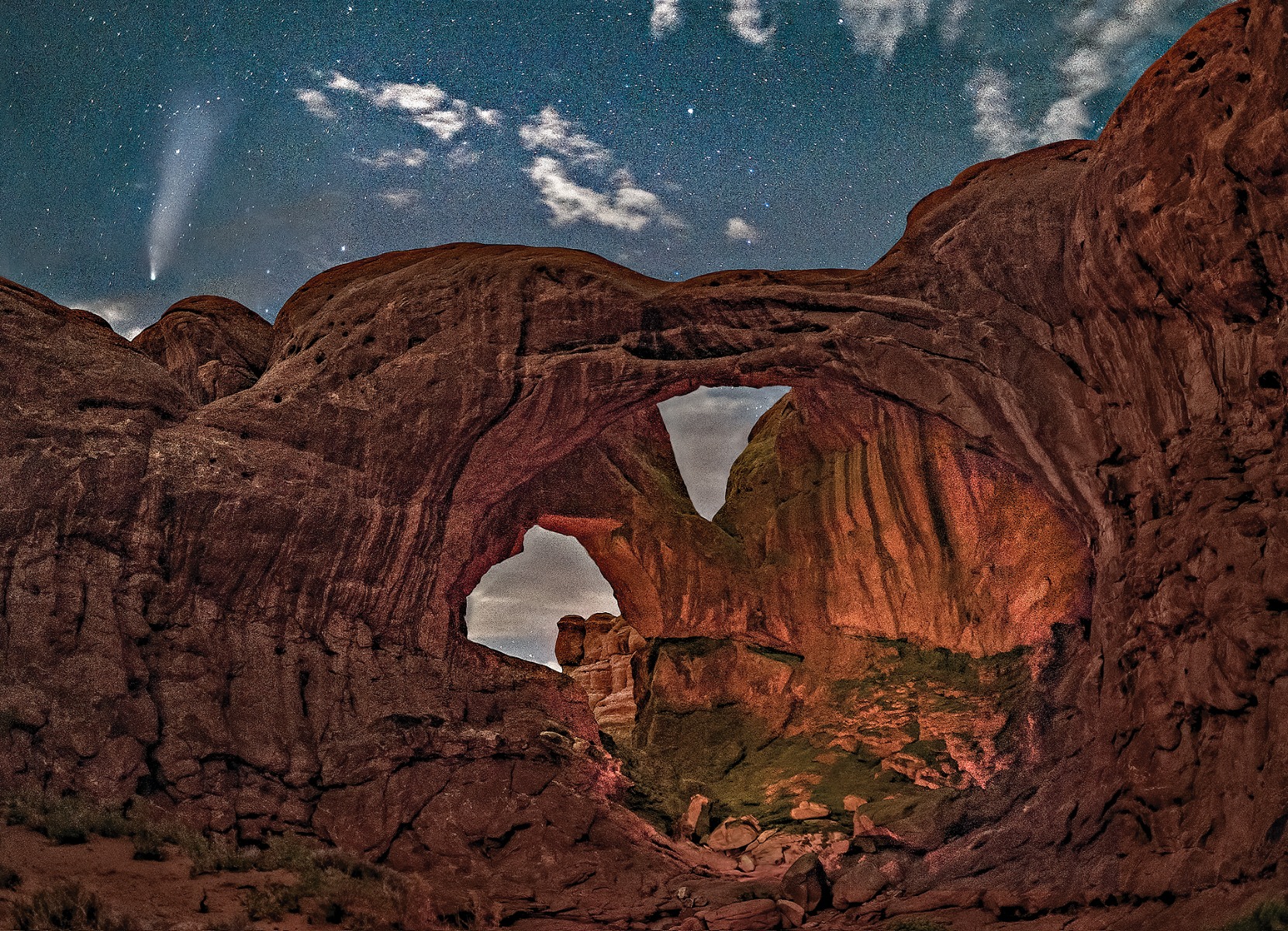 Comet NEOWISE streaks across the sky above Double Arch in Arches National Park during astronomical twilight, the darkest twilight stage.