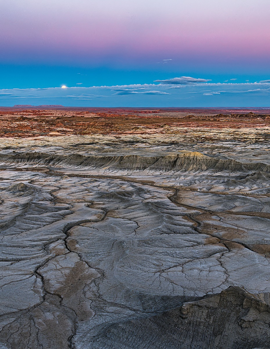 Partially shrouded by distant clouds, the full moon rises above the badlands near Hanksville during civil twilight.
